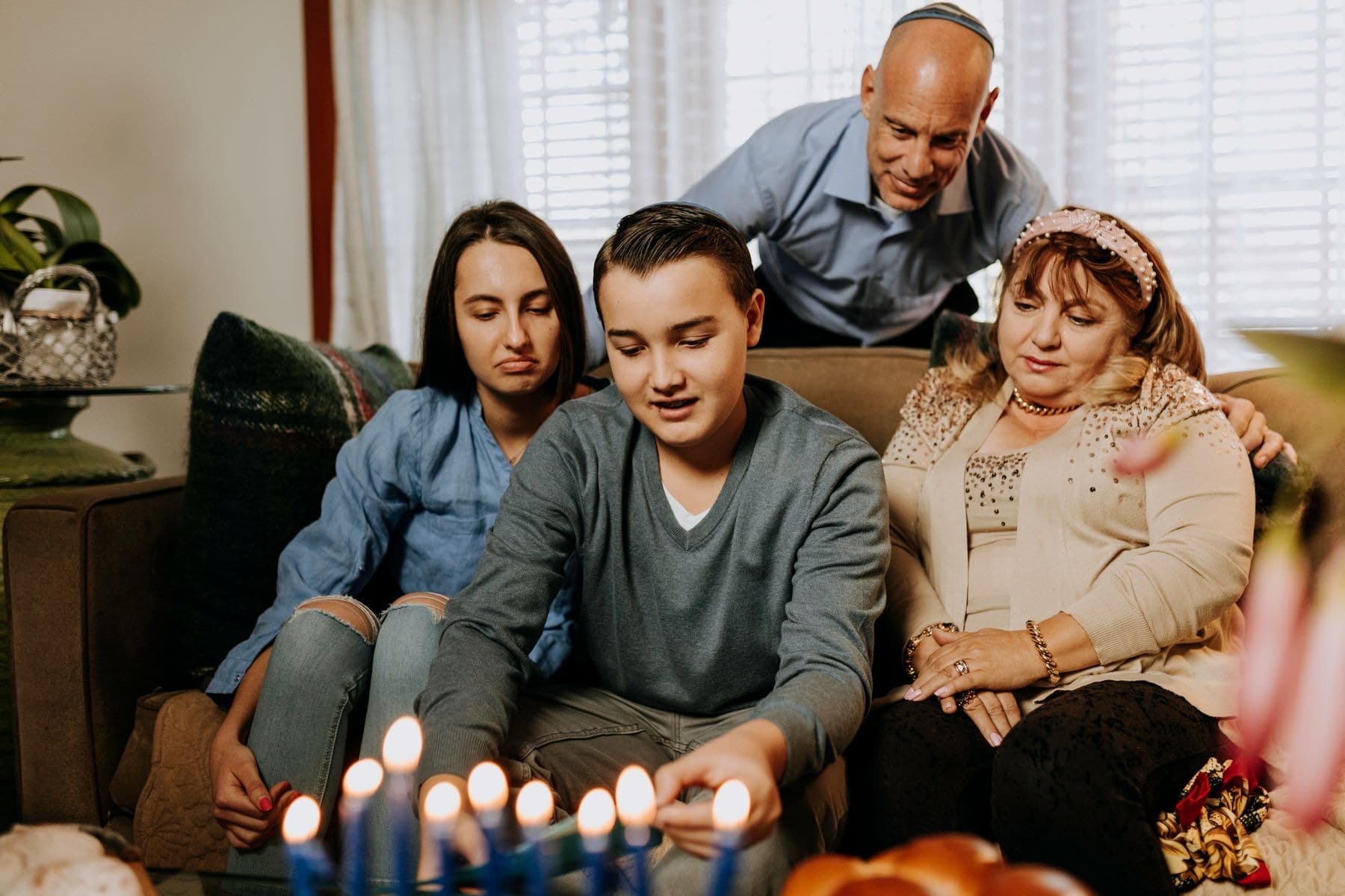 Family on a sofa watching a boy light the Chanukah menorah